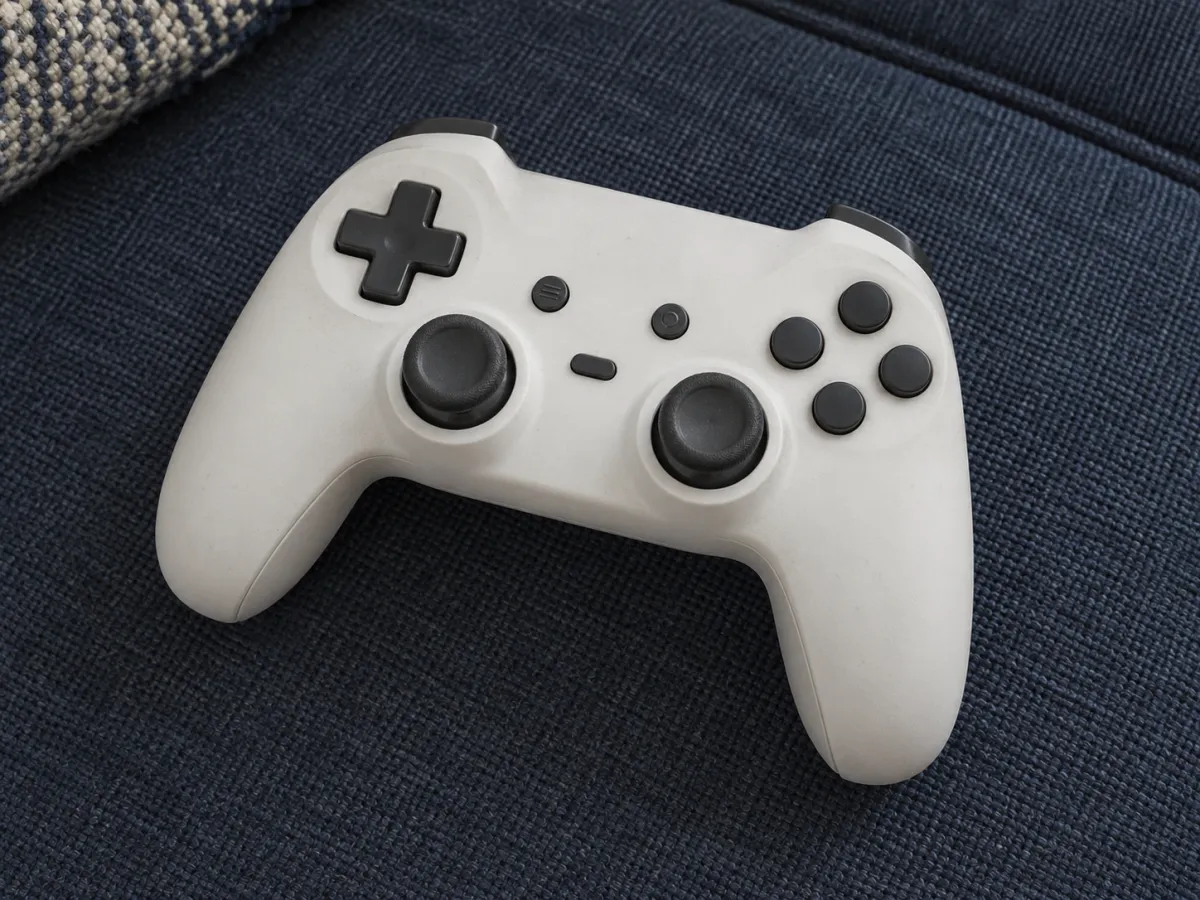 A matte off-white game controller with two thumbsticks resting on a blue fabric sofa seat.