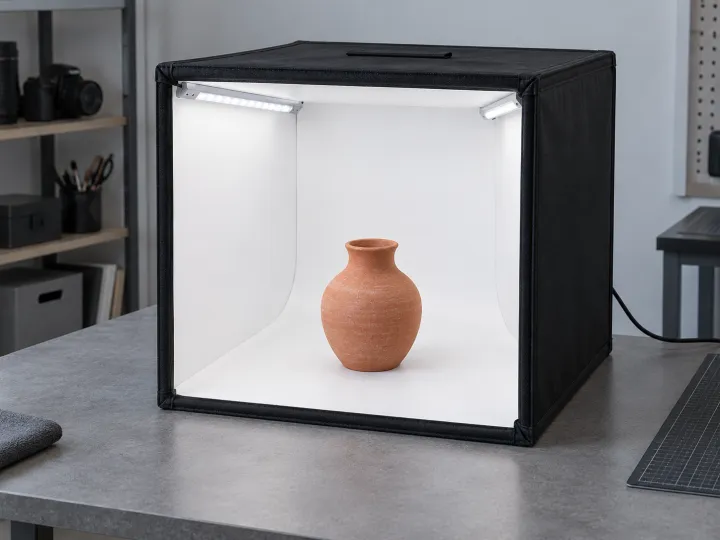 An open-front photography light box with mounted LED strips and a small terracotta vase inside.