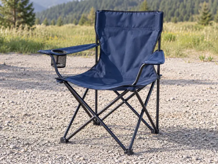 A navy folding camping chair with fabric arms, an empty cup holder and a steel scissor frame on level gravel.