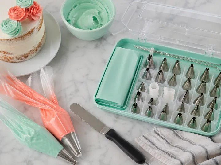 Piping bags, metal decorating tips and an offset spatula arranged beside a small iced cake.