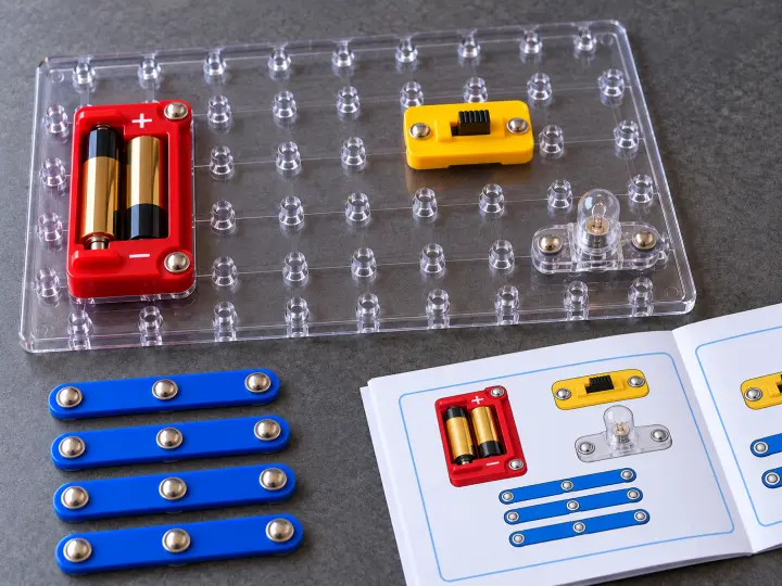 A battery holder, switch, lamp and loose snap-on strips laid out on a clear experiment board.