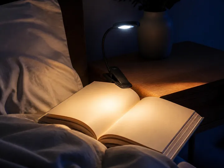 A small clip-on reading light illuminating the blank pages of an open book at night.
