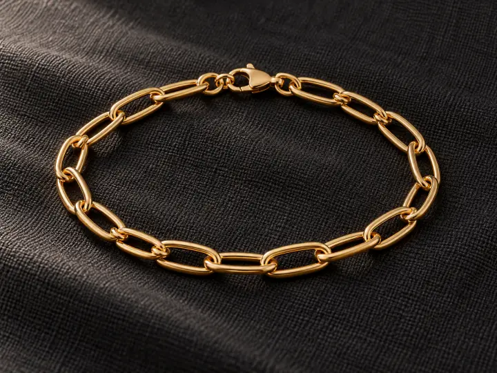 One gold-colored oval-link bracelet with a closed lobster clasp on dark woven cloth.