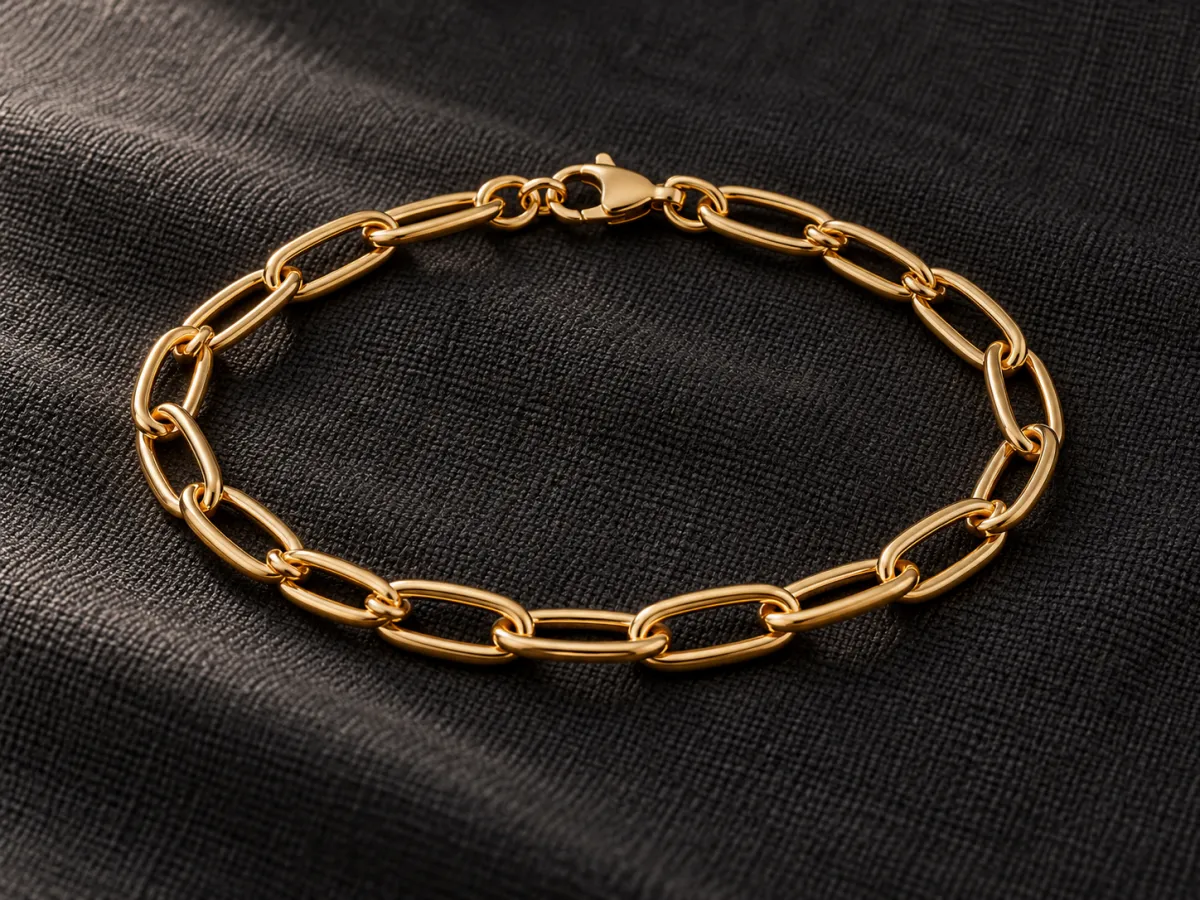 One gold-colored oval-link bracelet with a closed lobster clasp on dark woven cloth.