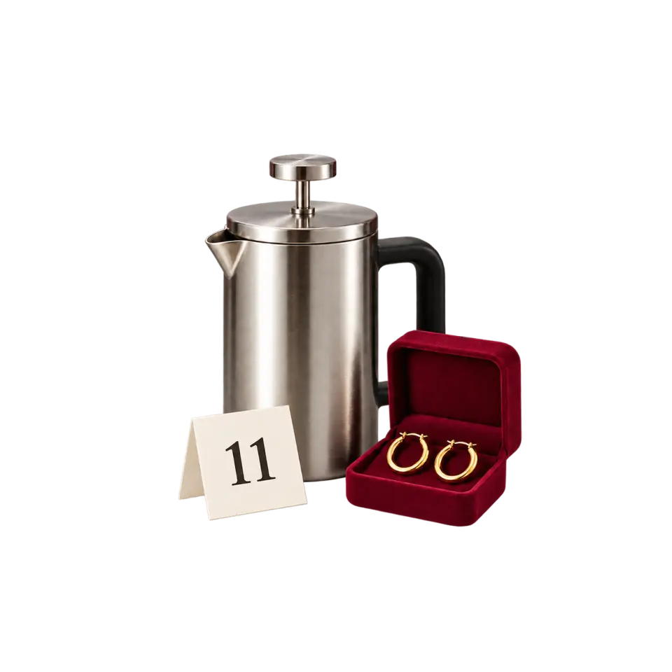 A stainless-steel cafetière beside gold-coloured hoop earrings in a burgundy box and a cream card marked 11.