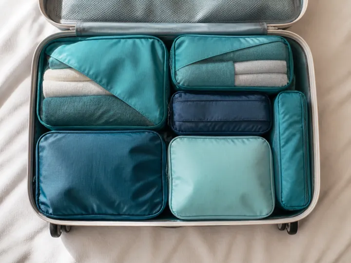 Teal packing cubes organizing folded clothes inside an open suitcase.